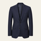 The Blazer in navy on a bone background, front view: single breasted, two buttons, notch lapel, welt chest pocket and flap hip pockets, tailored fit tapering at the waist