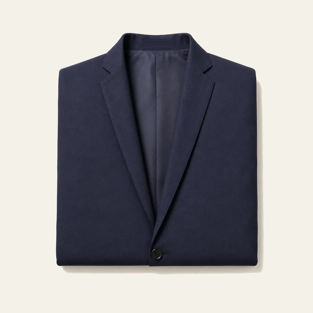The navy blazer folded flat on a bone background, showing both notch lapels, the lining and the top button