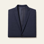 The navy blazer folded flat on a bone background, showing both notch lapels, the lining and the top button