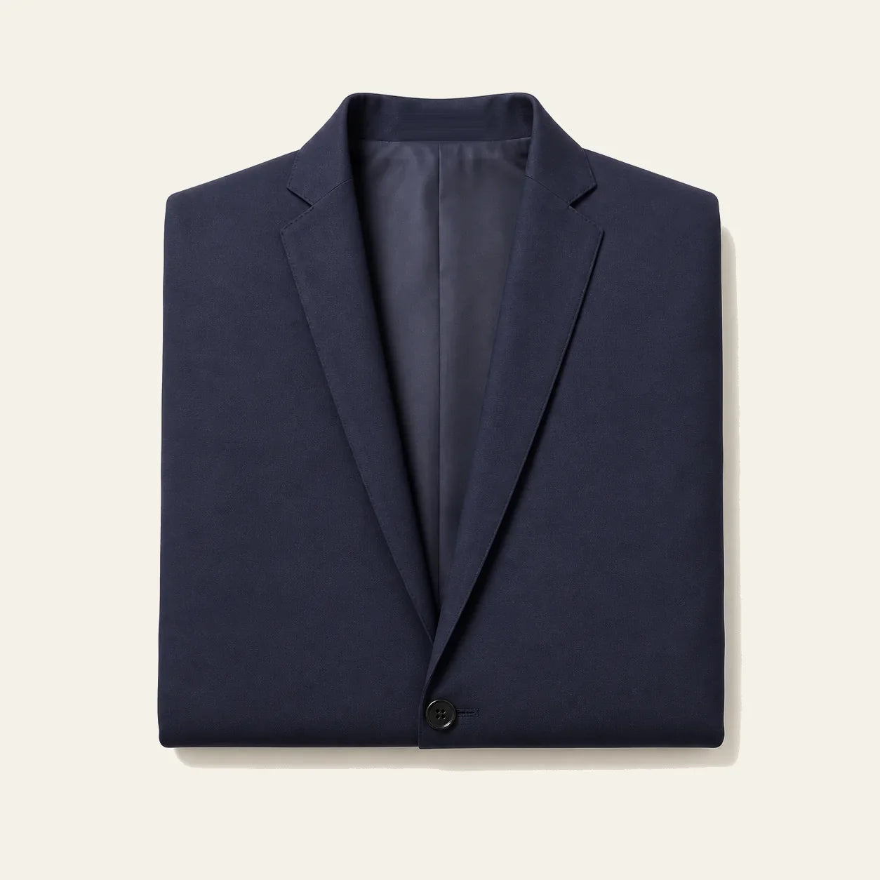The navy blazer folded flat on a bone background, showing both notch lapels, the lining and the top button
