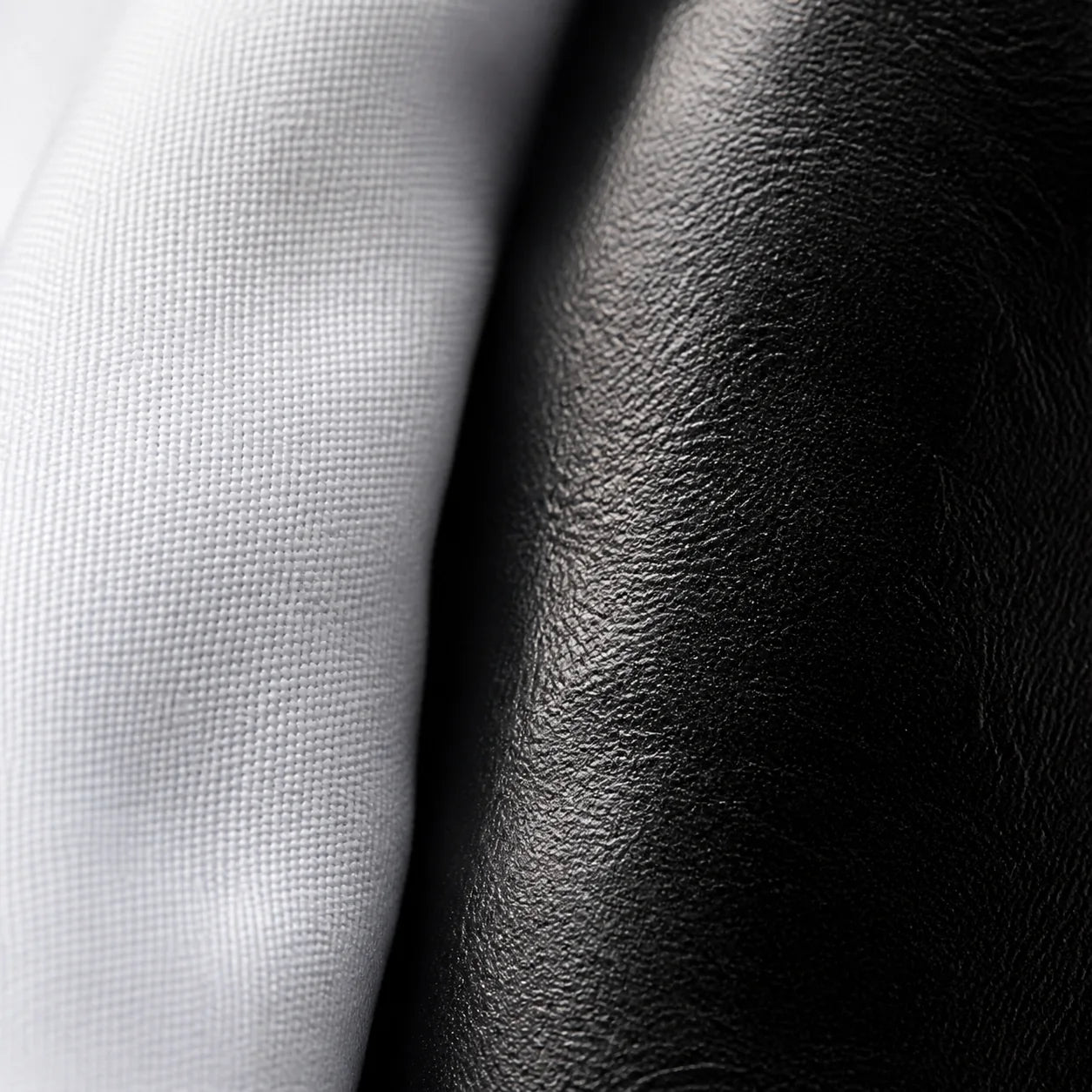 Macro close-up of white cotton shirt fabric meeting the grained black leather of the Chelsea boot, detail held in both extremes