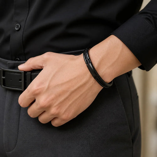 Close macro of a wrist wearing The Cuff in Black over a black shirt cuff, hand resting near a black leather belt