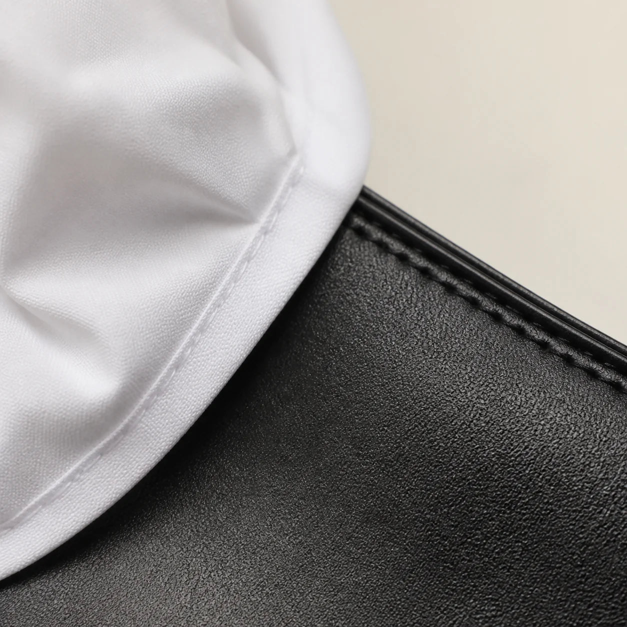 Macro close-up of white cotton shirt fabric meeting the grained black leather of the Chelsea boot