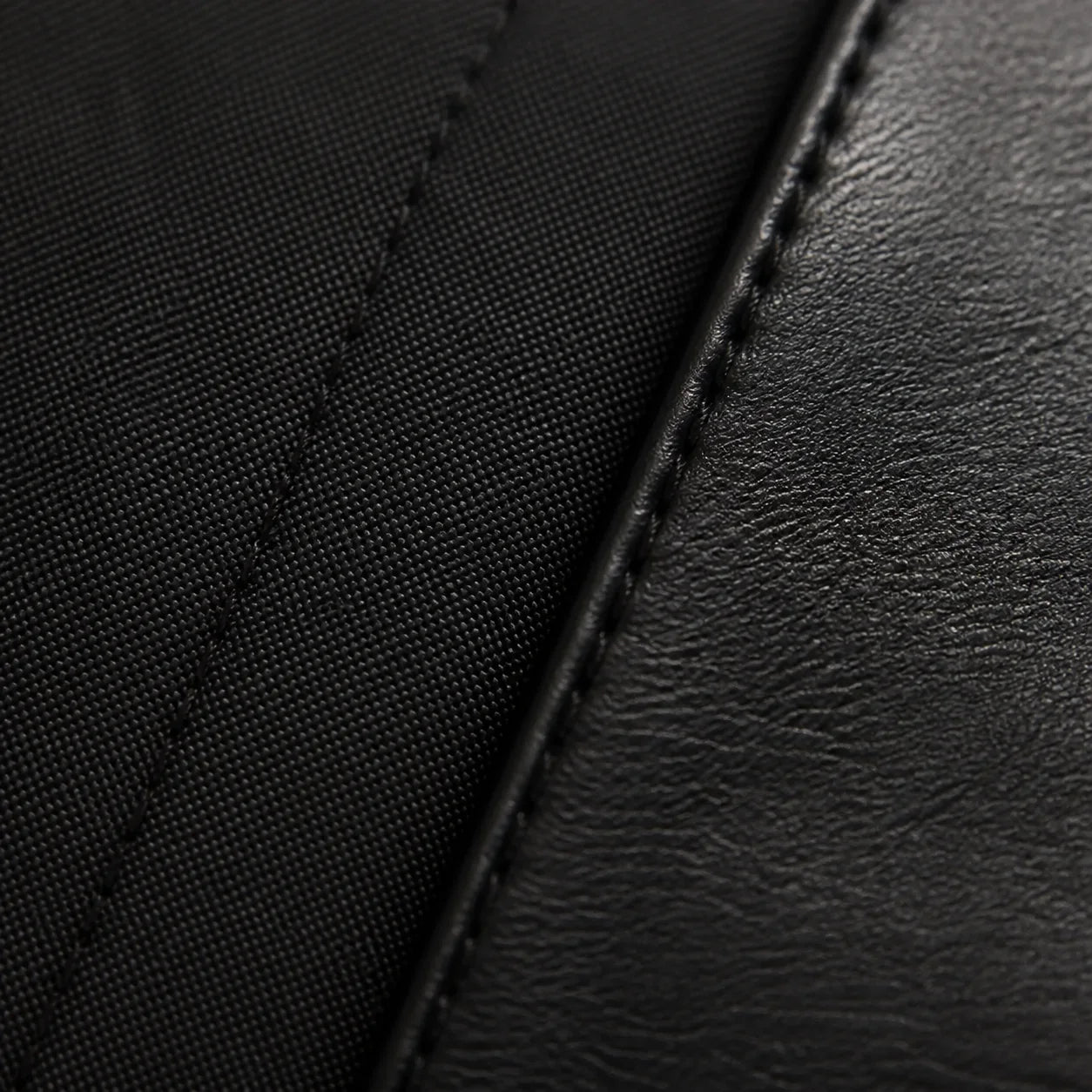Macro close-up of matte black cotton shirt fabric meeting the stitched black leather of the Chelsea boot