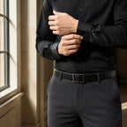Close crop of hands adjusting the cuff of a black shirt above charcoal trousers and a black leather belt