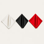 Three silk pocket squares side by side, Ivory, Black and Red, each a solid colour with a self-coloured rolled hem, on a bone background