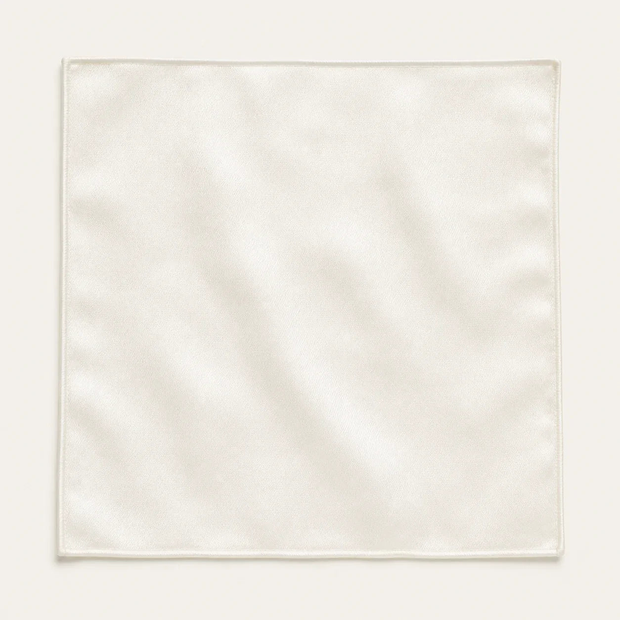 Solid ivory silk pocket square laid flat and open on a bone background, showing the full 34 by 34 centimetre square