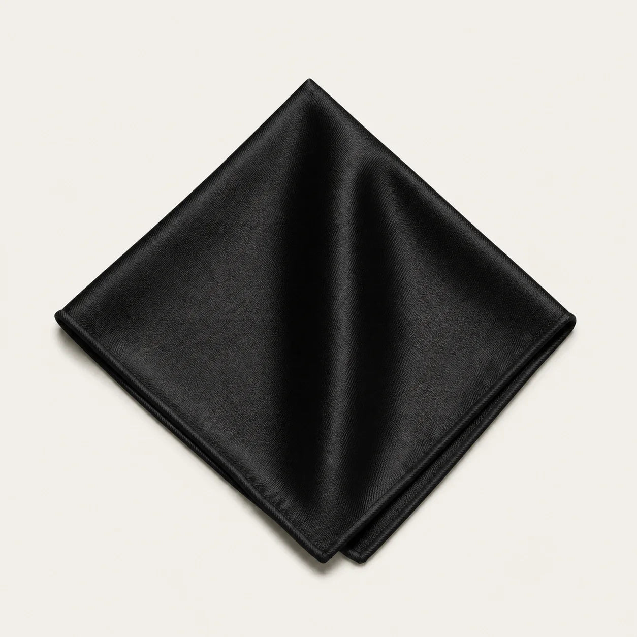 The Square in Black: solid black silk pocket square, folded, on a bone background
