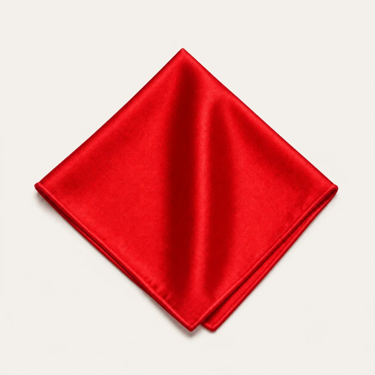 The Square in Red: solid red silk pocket square, folded, on a bone background