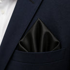 Close macro of the solid black pocket square folded into the breast pocket of the navy blazer, worn over a white shirt